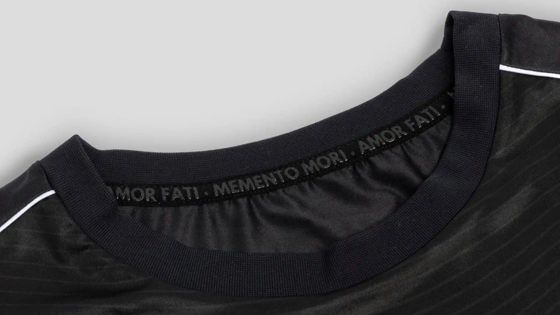 Black t-shirt collar with ’MEMENTO MORI’ text printed on the inner neckline.