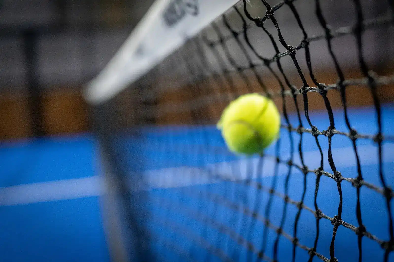 Tennis ball hitting against a black mesh net.