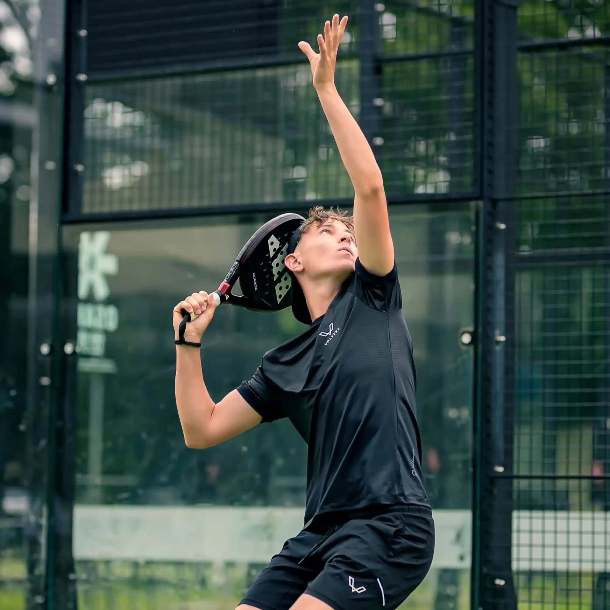 Tennis player serving in an all-black outfit.